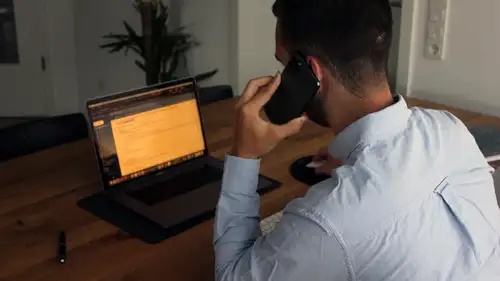 A man taking a call at his desk in front of a laptop